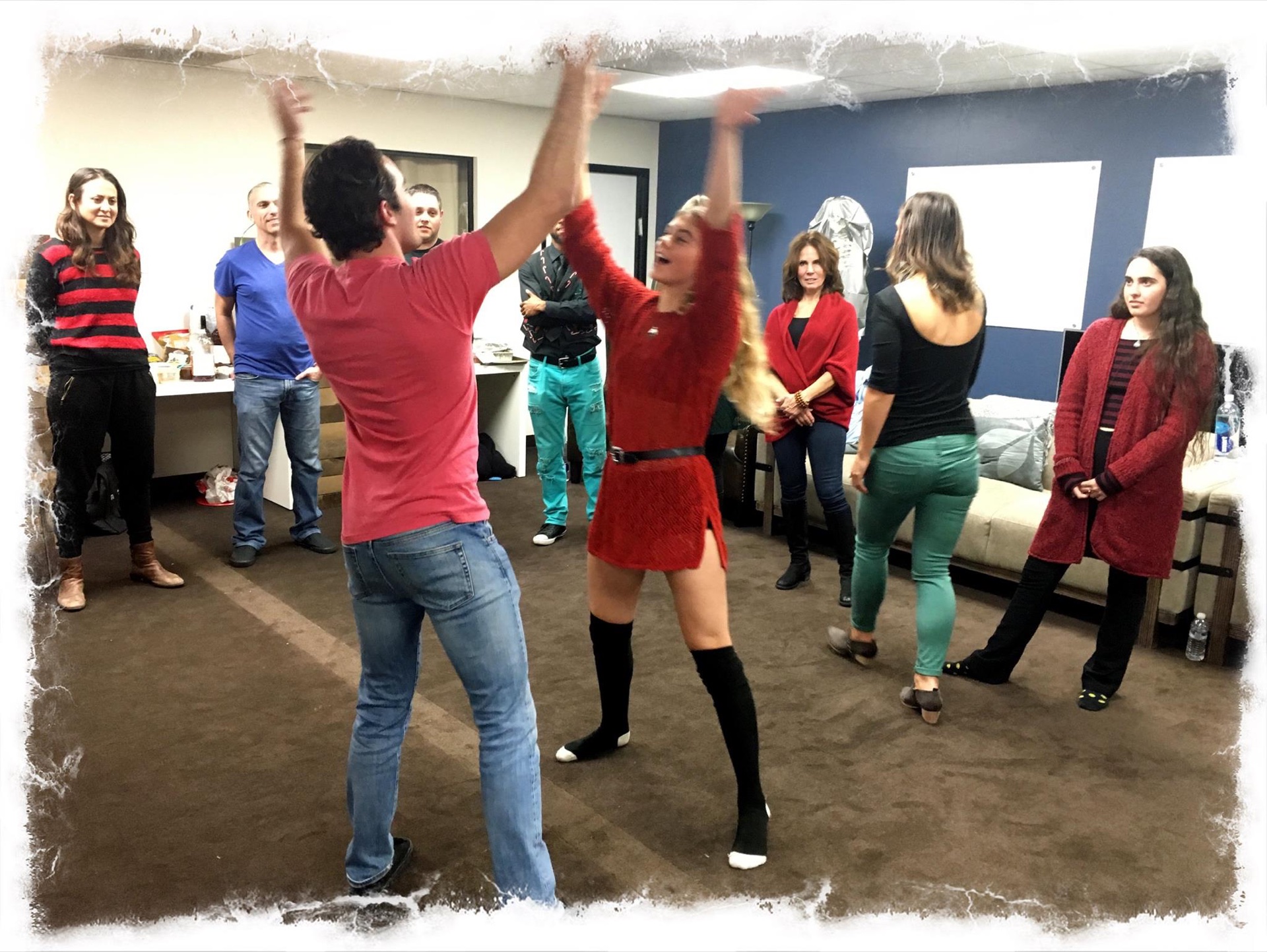 Two participants with arms raised high in an energetic improv exercise while others watch and cheer